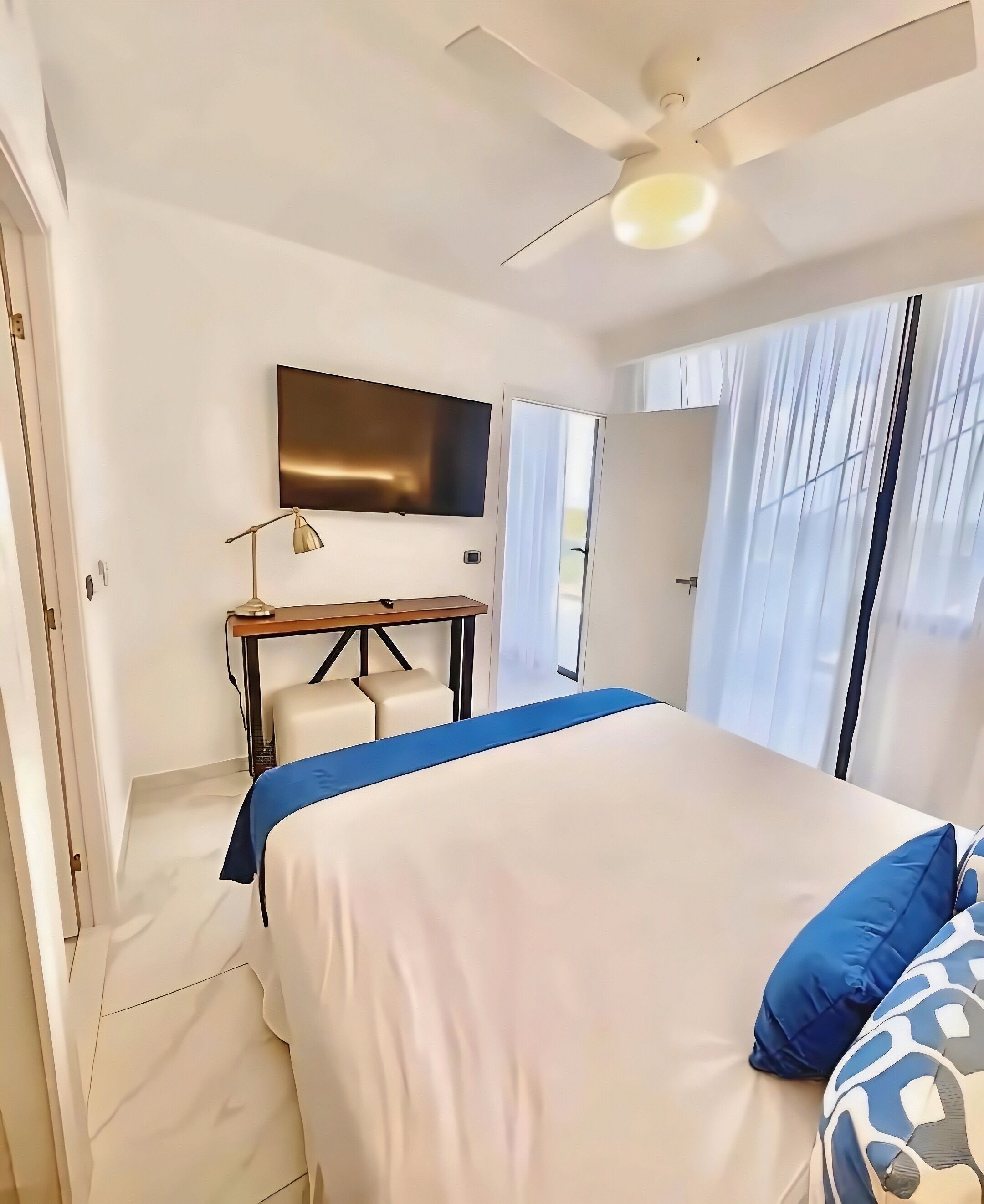 A bedroom with a bed, a desk, a television, and a ceiling fan.
