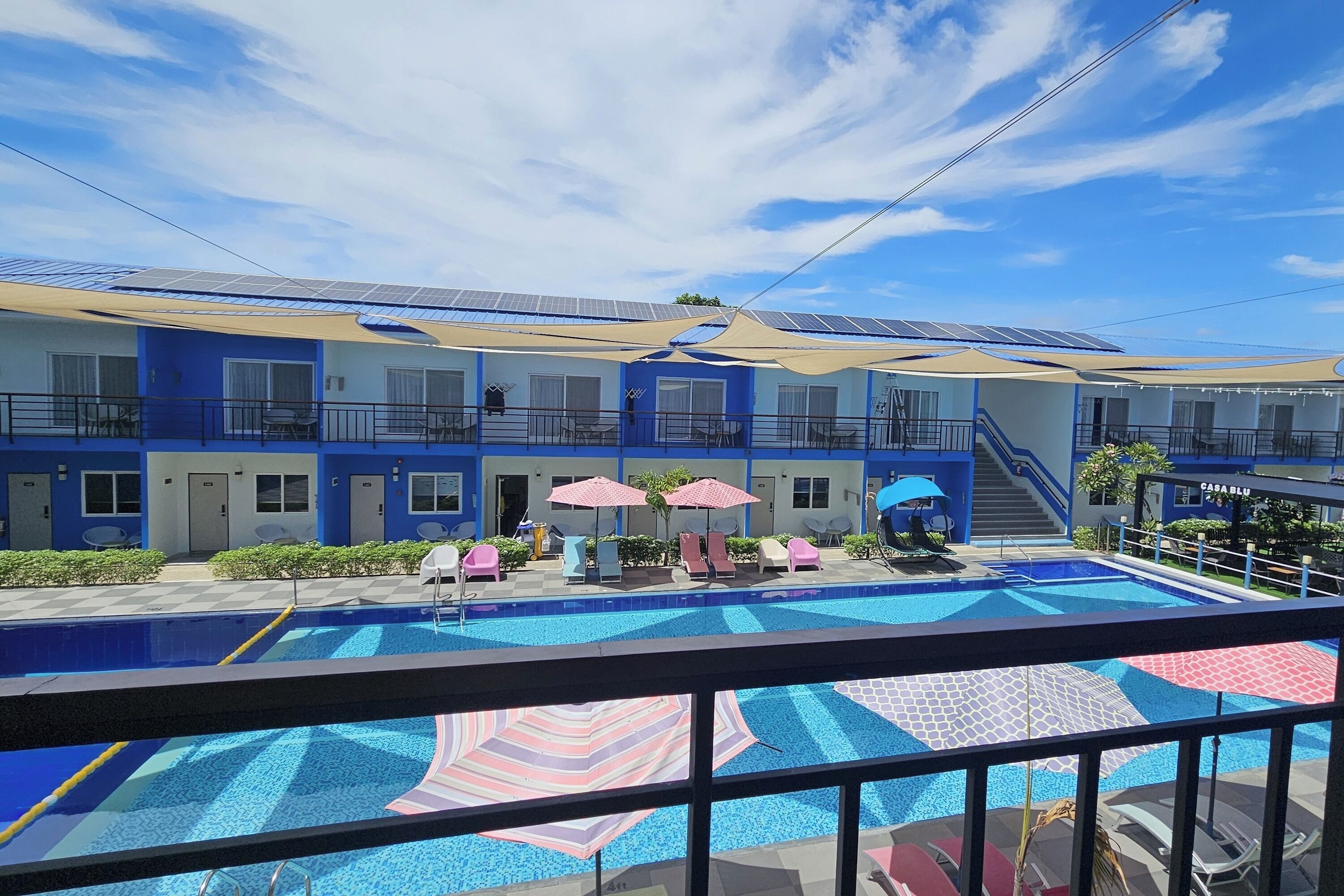 A hotel with a swimming pool, sun loungers, and a covered patio area.