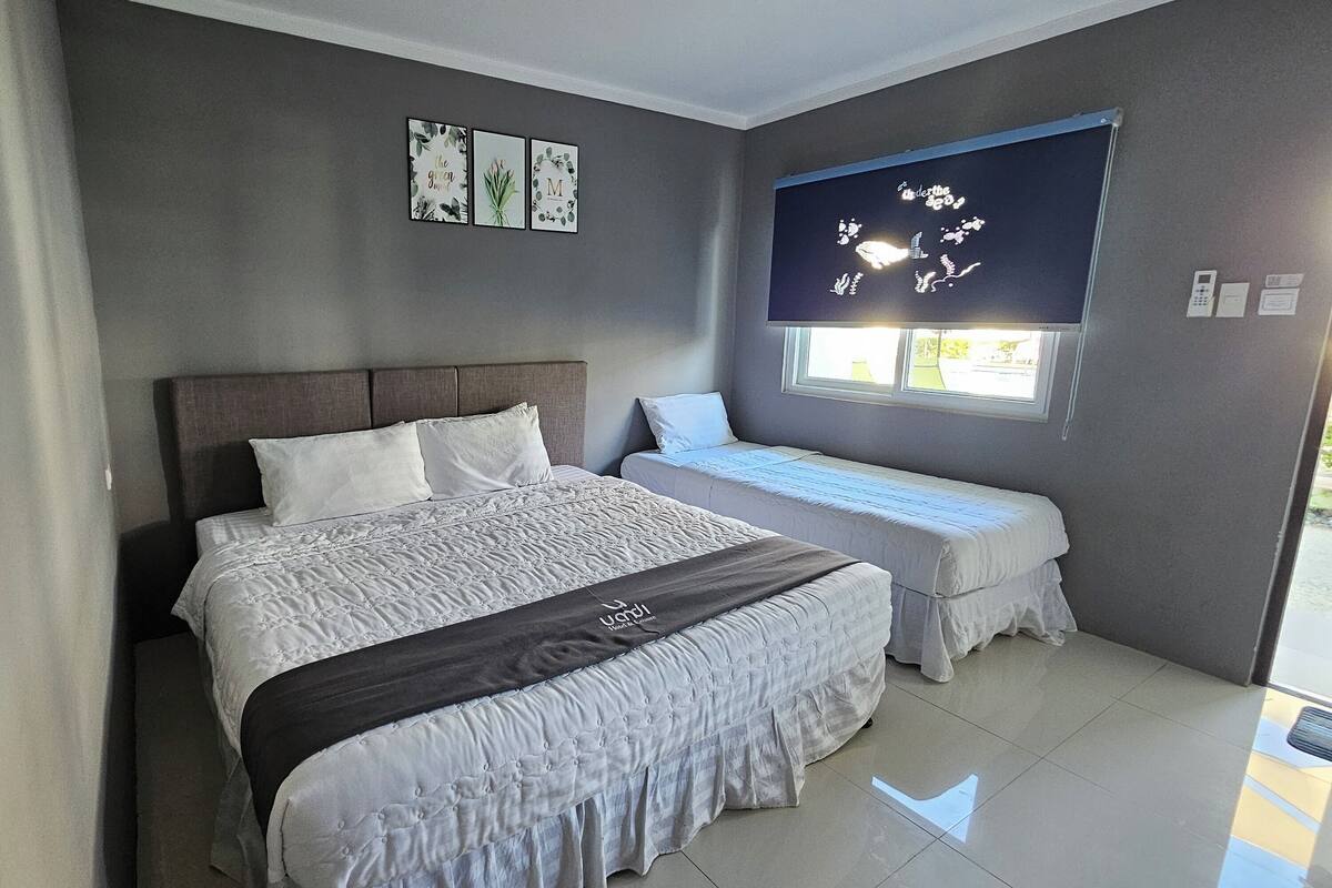 Un dormitorio con una cama grande, una cama más pequeña, una ventana con vistas y un televisor montado en la pared.