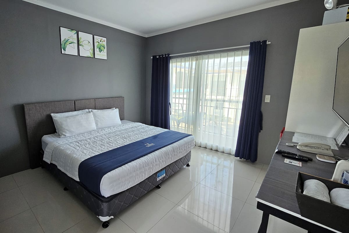 Habitación de hotel ordenada con cama, escritorio y ventana con cortinas.