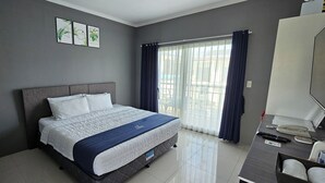 Ein ordentlich eingerichtetes Hotelzimmer mit Bett, Schreibtisch und einem Fenster mit Vorhängen.