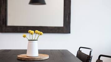 A white vase with yellow flowers on a round wooden coaster on a dark wooden table.