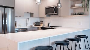 Eine moderne Küche mit Edelstahlgeräten, einer weißen Arbeitsplatte und schwarzen Barhocker.