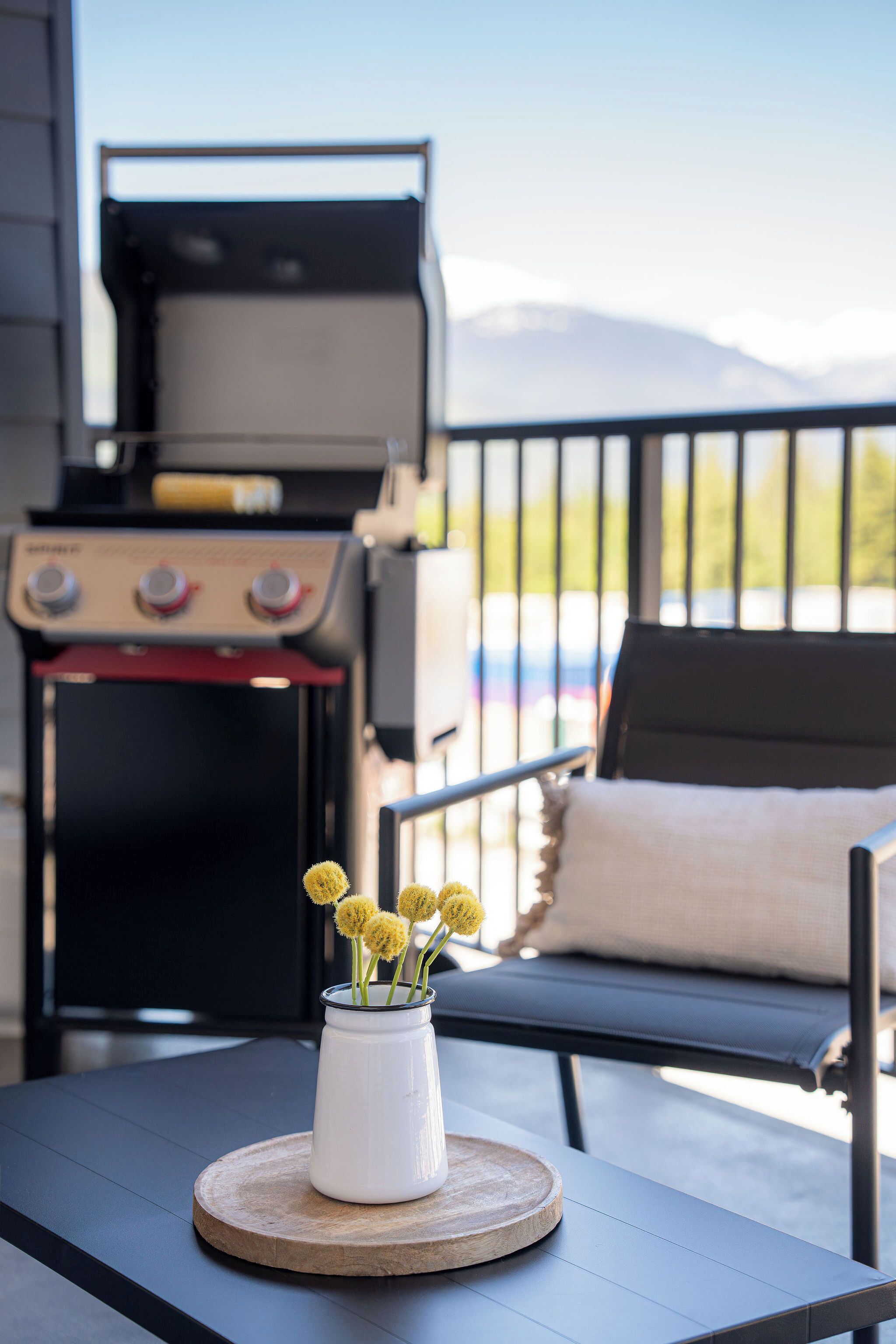 Une terrasse avec un barbecue, une table agrémentée d’un vase de fleurs et une chaise avec un coussin.