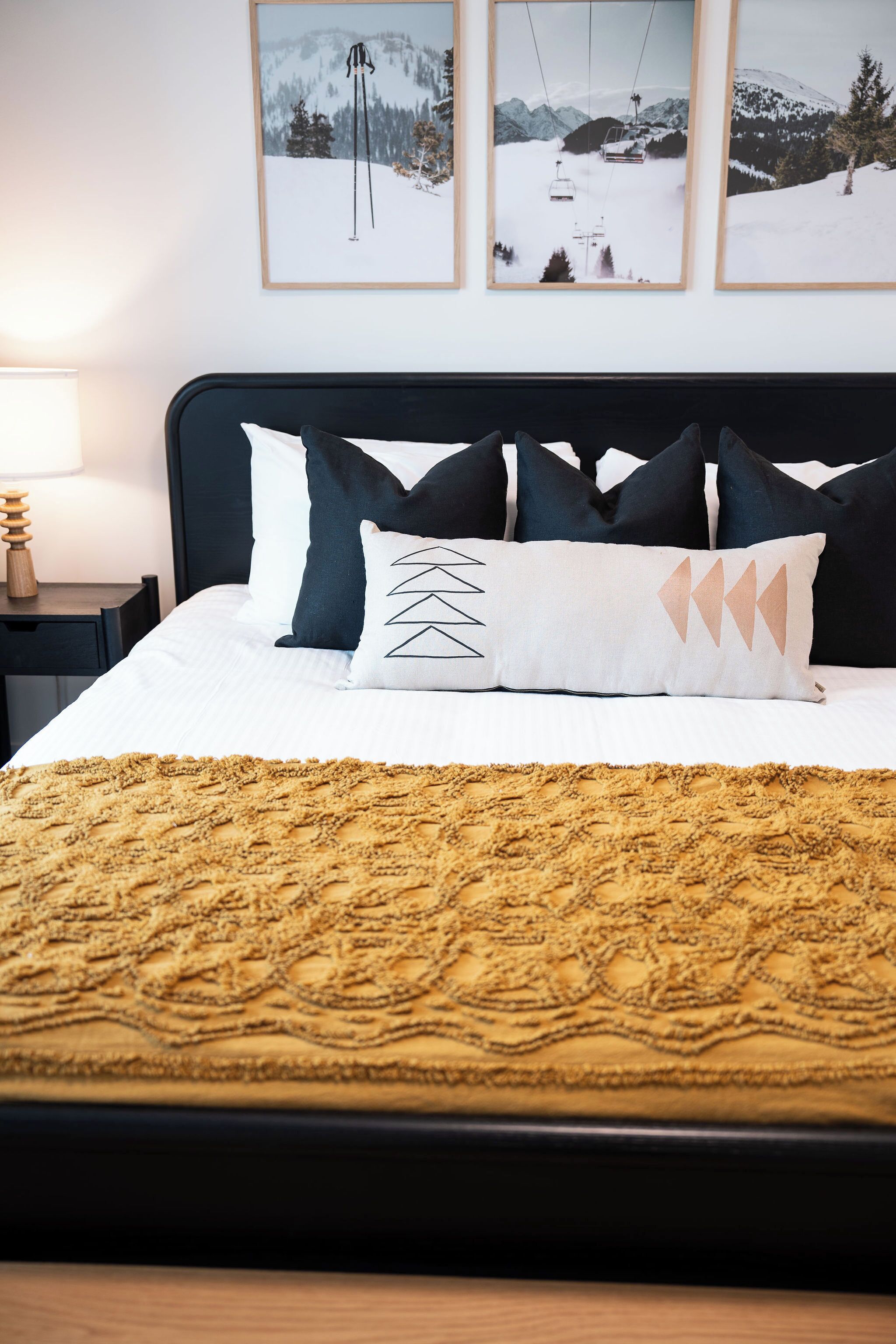 A neatly made bed with a patterned blanket, a black headboard, and multiple pillows.