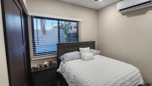 Een slaapkamer met een bed, nachtkastje, raam met zonwering en een airconditioning.