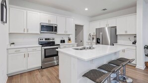 A modern kitchen with white cabinetry, stainless steel appliances, and a central island with bar stools. - Retreat at Louisiana State Capitol by LSU - CB1016 (Baton Rouge)