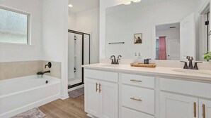 A modern bathroom with a bathtub, a large vanity with a mirror, and a shower area. - Retreat at Louisiana State Capitol by LSU - CB1016 (Baton Rouge)