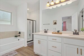 A modern bathroom with a bathtub, a large vanity with a mirror, and a shower area. - Retreat at Louisiana State Capitol by LSU - CB1016 (Baton Rouge)