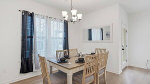 A dining area with a wooden table and chairs, a chandelier, and a window with curtains. - Retreat at Louisiana State Capitol by LSU - CB1016 (Baton Rouge)