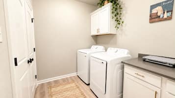 A laundry room with two front-loading washing machines, a drying rack, and a small desk with a keyboard.