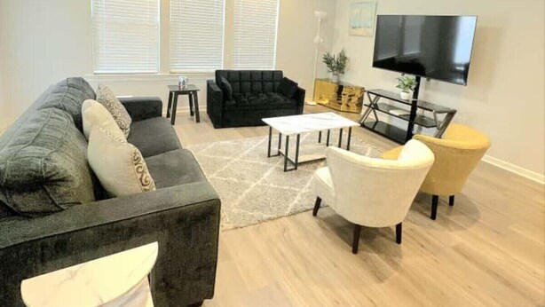 A modern living room with a sectional sofa, a white armchair, a coffee table, and a flat-screen TV mounted on the wall. - Retreat at Louisiana State Capitol by LSU - CB1016 (Baton Rouge)