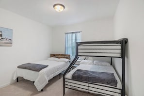 A bedroom with two single beds, a window with curtains, and a painting on the wall.