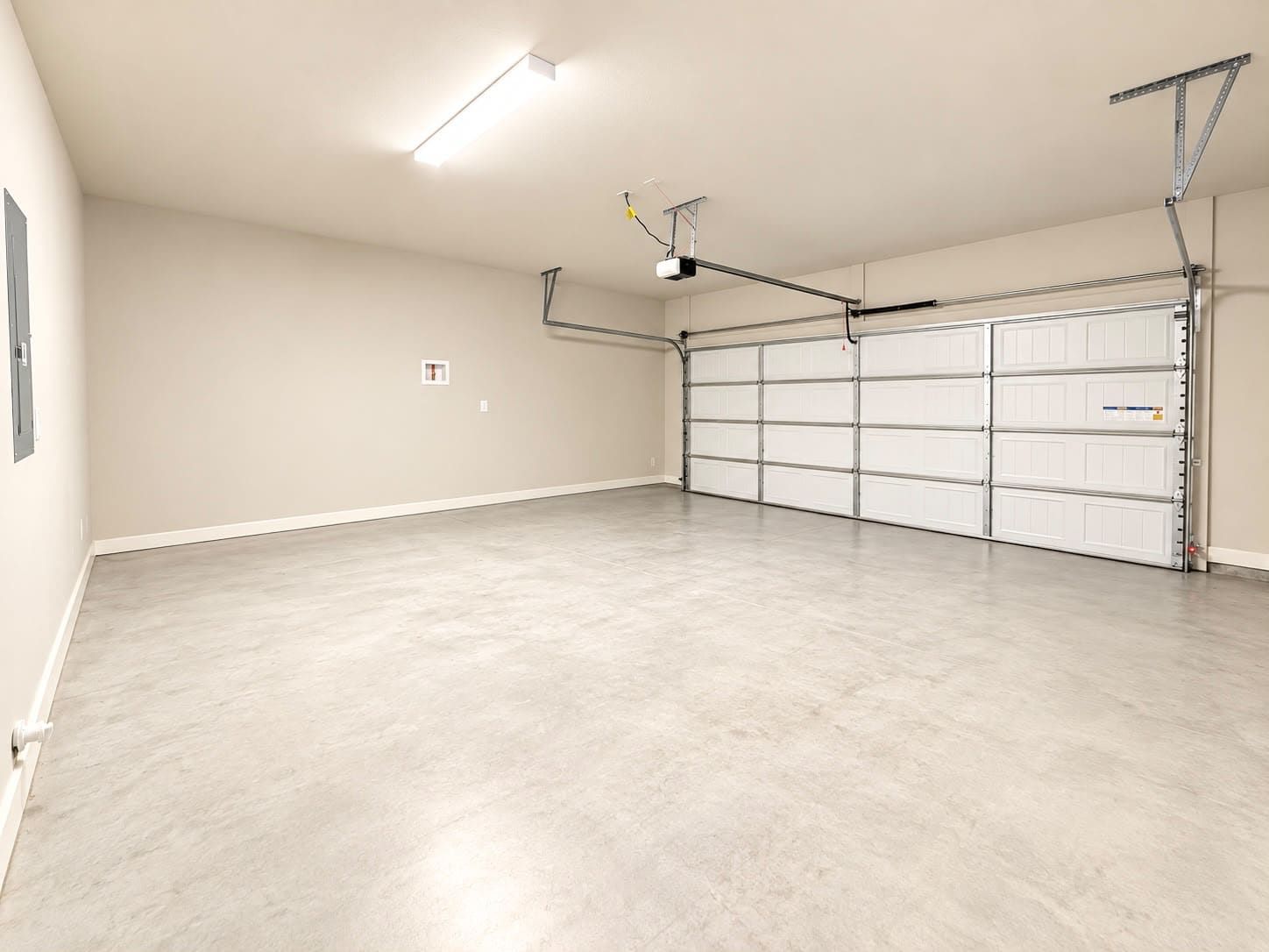 Un garaje espacioso con piso de concreto, una puerta grande de color blanco e iluminación en el techo.