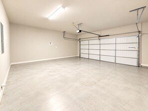 A spacious garage with a concrete floor, a large white garage door, and overhead lighting. - Retreat at Louisiana State Capitol by LSU - CB1016 (Baton Rouge)