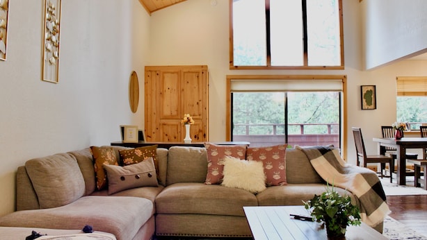 A cozy living room with a sectional sofa, a dining table, and a large window offering a view of trees.