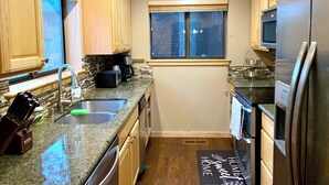 A compact kitchen with wooden cabinets, a stainless steel refrigerator, a built-in oven, and a window.