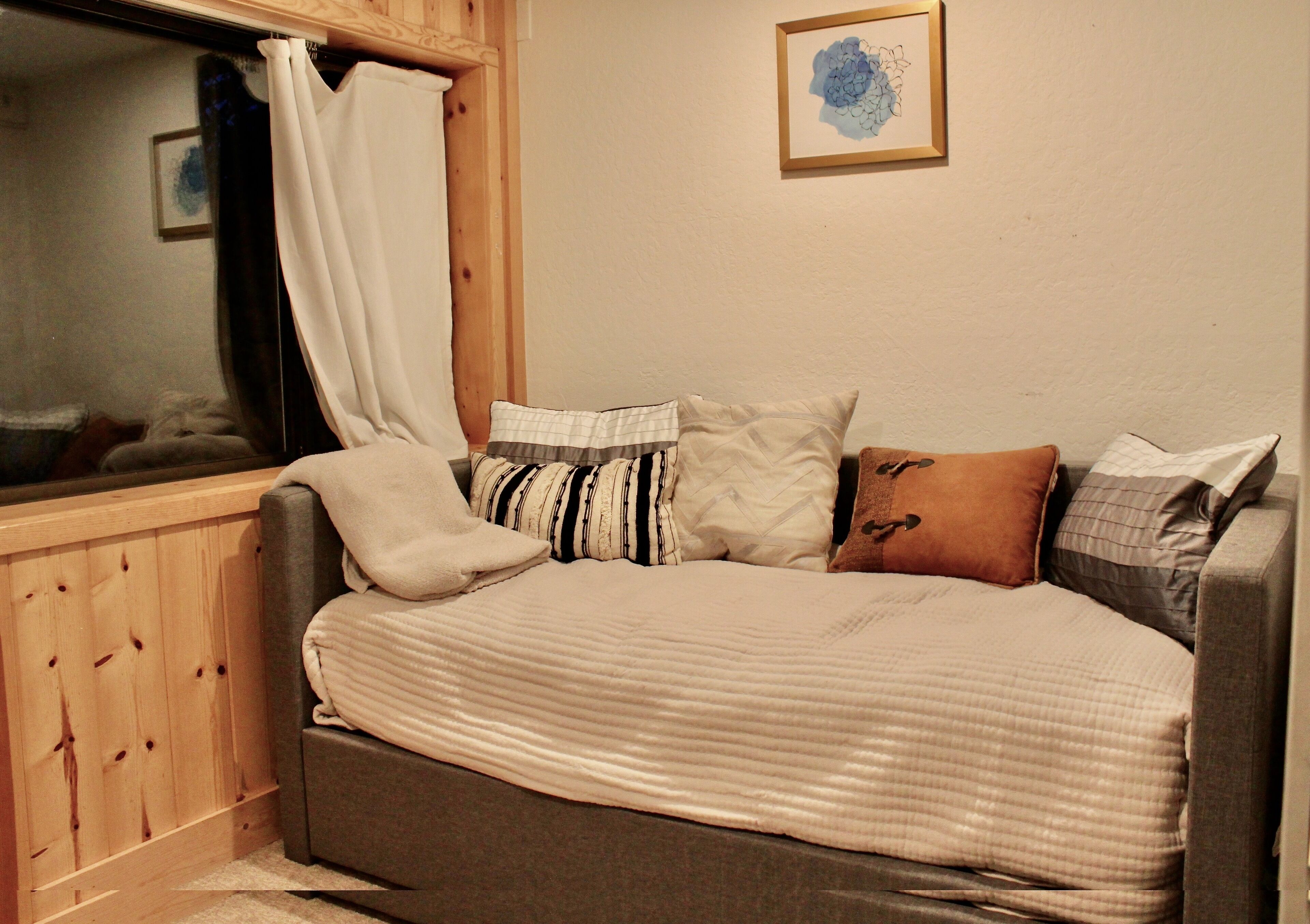 A cozy bedroom with a bed, a window with curtains, a framed picture on the wall, and a wooden headboard.