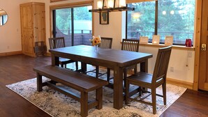 A dining area with a wooden table and benches, large windows, and a view of trees.