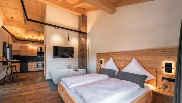 A modern bedroom with a wooden bed, a built-in TV, and a small bathroom. - Apartment "Georg" 43 sqm with balcony (Traunstein)