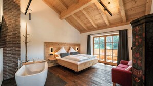 A bedroom with a large bed, a wooden headboard, a red chair, a white bathtub, and a window with curtains. - Apartment "Georg" 43 sqm with balcony (Traunstein)