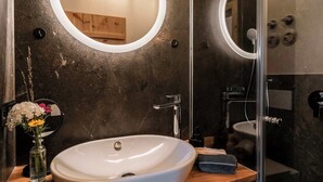 A bathroom with a wooden vanity, a white sink, a round mirror, and a glass shower enclosure. - Apartment "Georg" 43 sqm with balcony (Traunstein)