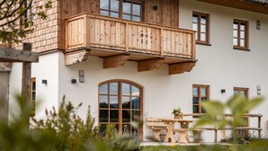 Un edificio de dos pisos con un balcón de madera, ventanas amplias y un jardín con un banco.