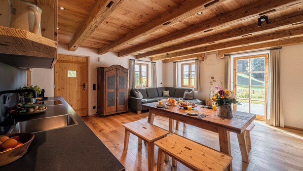 Una cocina amplia con vigas de madera, una zona de comedor con bancos y un gran ventanal con vistas al exterior.
