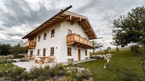 Un chalet de dos pisos con balcones de madera, un camino de piedra y un jardín con flores.