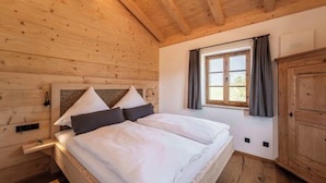 A wooden cabin bedroom with a bed, a window with curtains, and a wooden wardrobe.