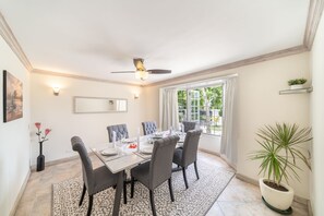 Une salle à manger avec une table dressée pour quatre personnes, un ventilateur de plafond et une plante en pot.