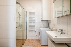 Ein kleines Badezimmer mit einer Duschkabine aus Glas, einer Waschmaschine und einem Waschbecken mit Spiegel darüber.