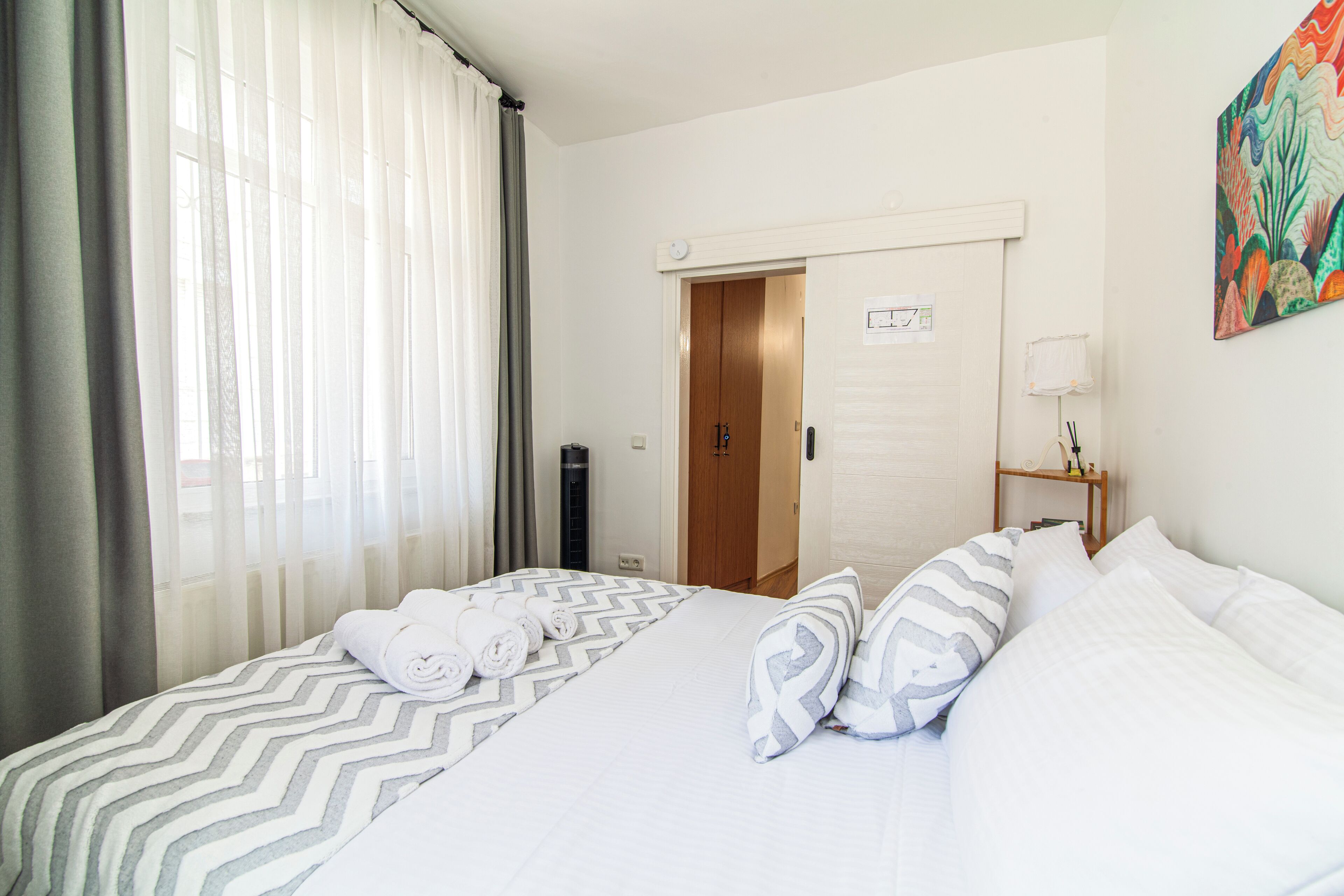 A hotel room with a bed, a nightstand, a door, and a painting on the wall.