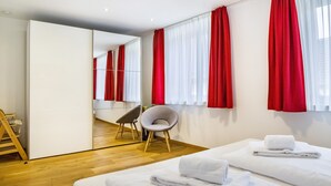 Una habitación de hotel con una cama, una silla, un espejo y cortinas rojas.