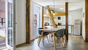 Un comedor con mesa y sillas, una cocina al fondo y estructura de vigas de madera.