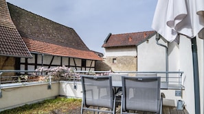 Un cortile con tavolo e sedie, un ombrellone bianco e edifici con tetti in tegole rosse.