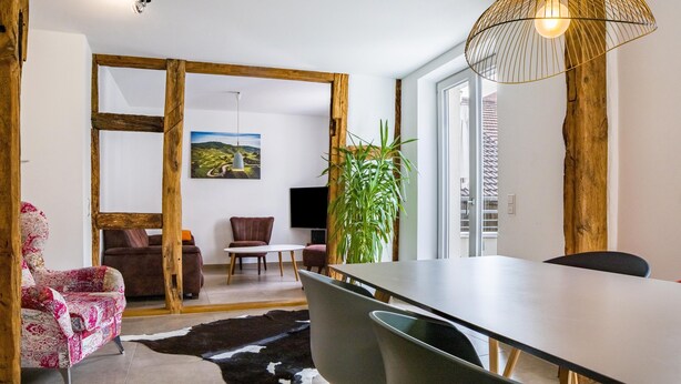 Un comedor moderno con puerta de madera, una mesa de comedor, sillas, un sofá, un televisor y una planta grande.
