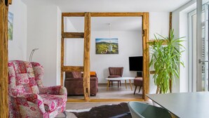 Una sala de estar con un separador de madera, un sillón estampado, un sofá, una mesa de comedor y una planta verde grande.