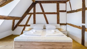 Une chambre avec une structure de plafond en bois, un lit recouvert de draps blancs et des tables de chevet avec des lampes.