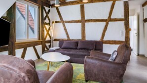 Une pièce avec des poutres apparentes, un canapé marron, deux fauteuils et une petite table blanche.