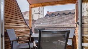 Un balcon en bois, agrémenté d’une table et de chaises, donnant sur un quartier résidentiel avec des bâtiments de style traditionnel.