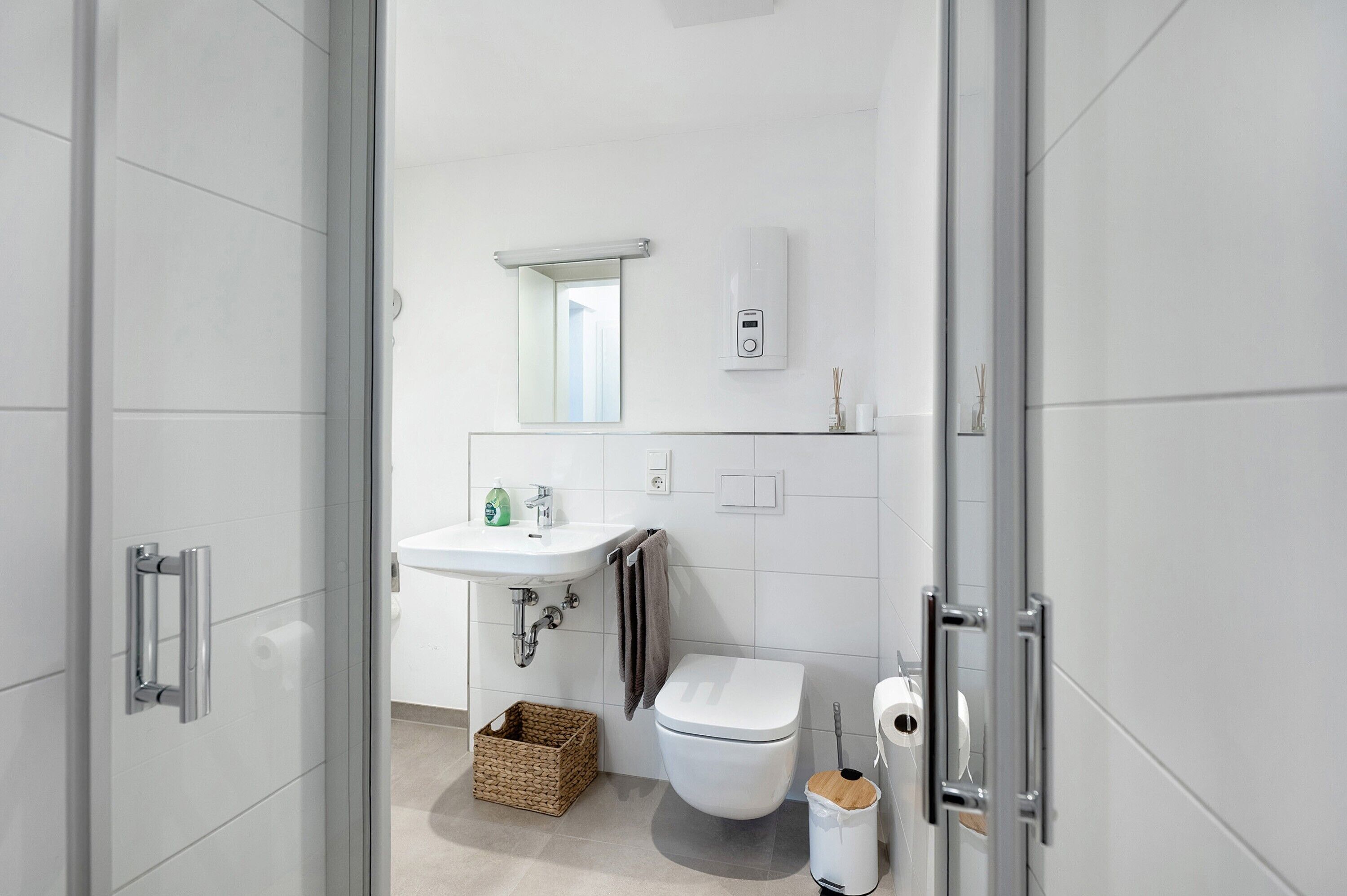 Une salle de bain moderne avec une douche à parois de verre, un lavabo blanc, des toilettes et une petite poubelle.
