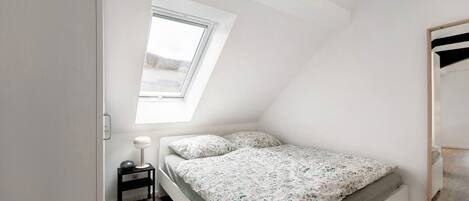 A bedroom with a skylight, a bed with floral bedding, a bedside table with a lamp, and a mirror on the wall.