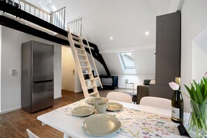 Une cuisine moderne avec un réfrigérateur en acier inoxydable, une table à manger dressée avec des assiettes et une bouteille de vin, et une échelle en bois menant à un niveau supérieur.