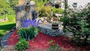 Un jardín con una estructura de piedra, un pérgola y una casa al fondo.
