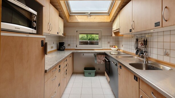 Una cucina compatta con mobili in legno, un forno a microonde integrato, una finestra a soffitto e una finestra.