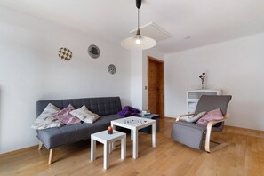 Un salon avec un canapé gris, une table basse blanche, un fauteuil gris et un plancher en bois.