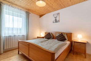 Un lit en bois avec une tête de lit, des tables de chevet avec des lampes, un radiateur et une fenêtre avec des rideaux légers.