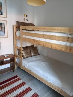 Un lit superposé avec une structure en bois, une literie blanche et un tapis rayé sur le sol.
