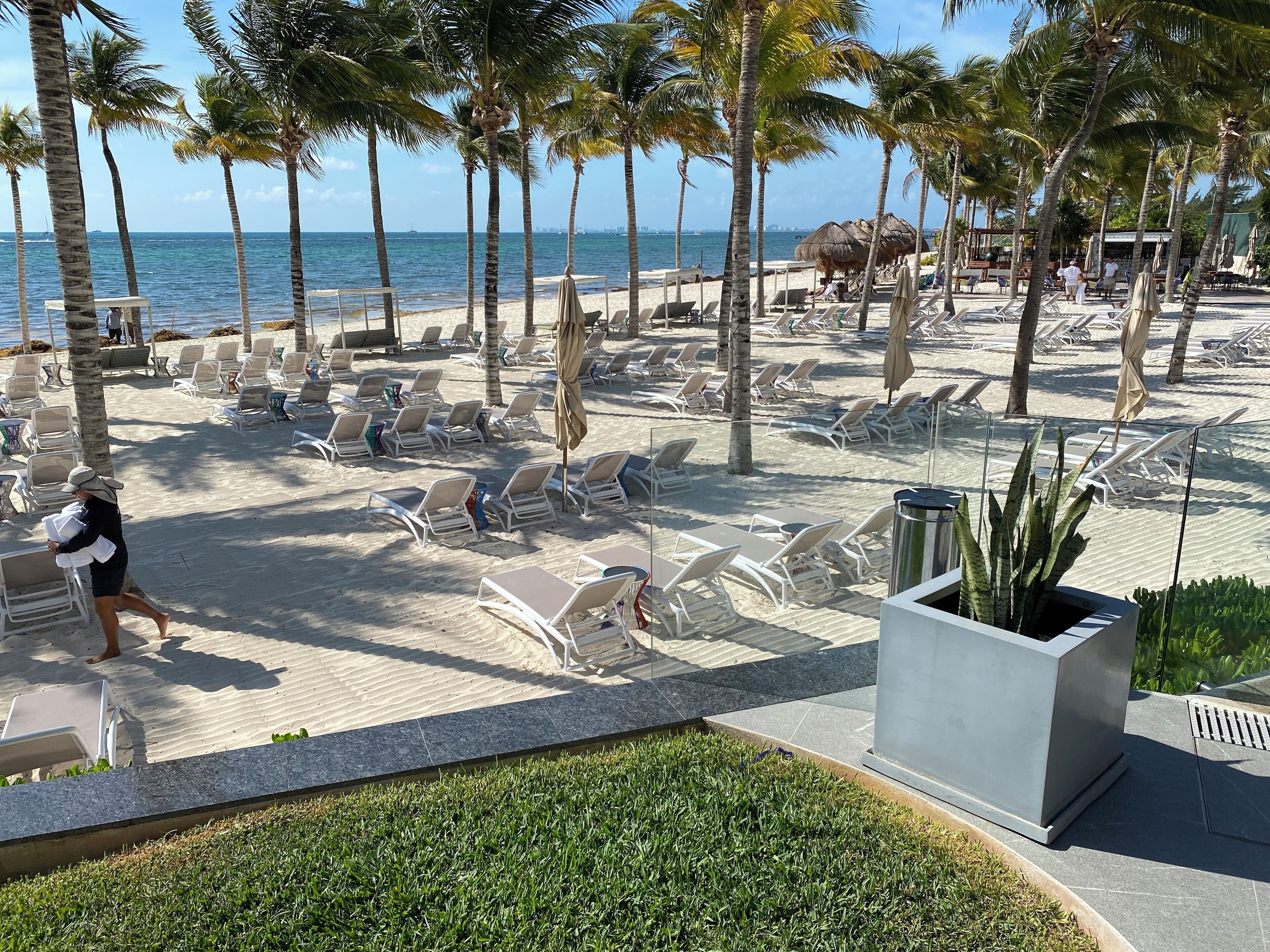 Un hôtel situé en bord de mer, doté de chaises longues, de palmiers et offrant une vue sur l’océan.